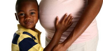 Adorable African American boy hugging expecting mom's belly over white background.