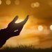 Silhouette of human hand with open palm praying to god at sunset background