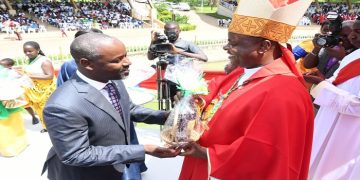 Deputy Speaker Thomas Tayebwa (L) hands over offertory to Lambert Bainomugisha, the Mbarara Archbishop.