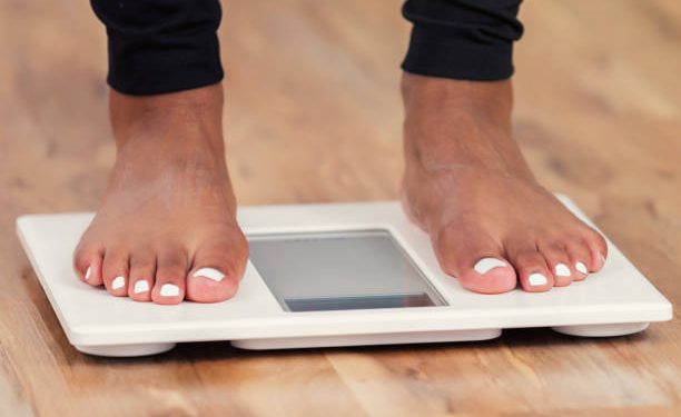 Unrecognizable woman checks her weight by standing on a bathroom scale.
