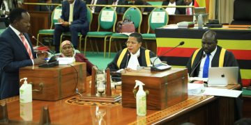 Hon. Wilson Kajwengye (L) speaking during the sitting on Tuesday. Speaker Anita Among (C) and a staff member of Parliament (R) are at the Clerk’s Table.